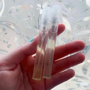 Pu&ograve; includere: Due flaconi di campioni di profumo trasparenti e rettangolari con vaporizzatori trasparenti. I flaconi contengono un liquido giallo chiaro. Lo sfondo &egrave; una finestra in vetro smerigliato con un motivo floreale.