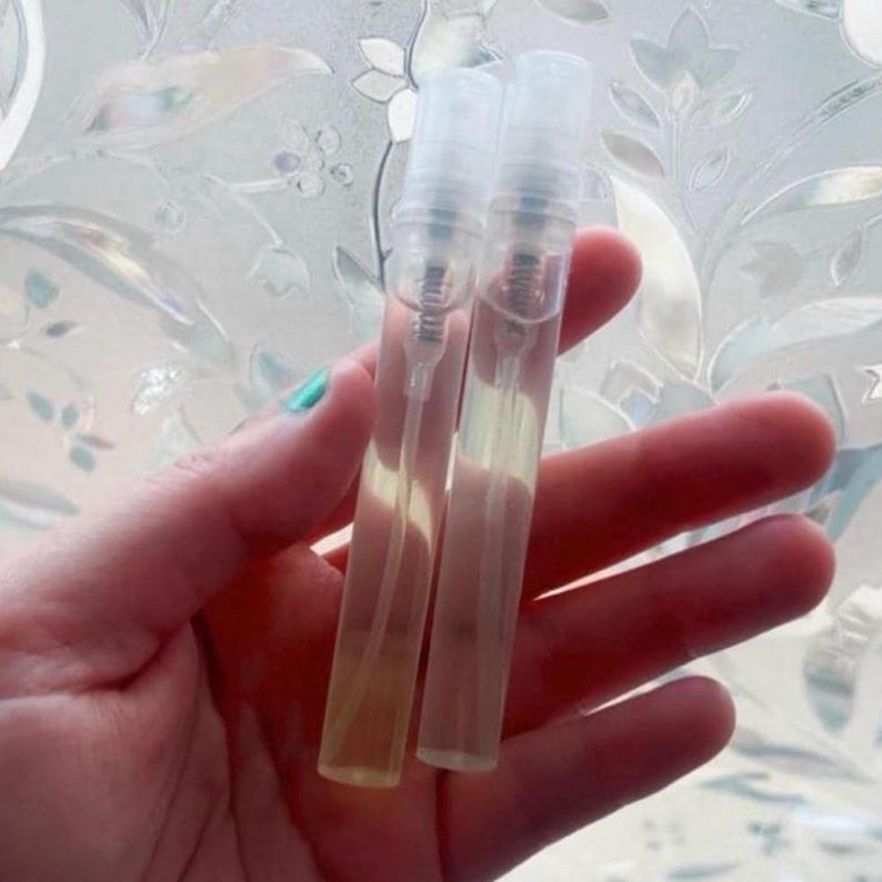 Pu&ograve; includere: Due flaconi di campioni di profumo trasparenti e rettangolari con vaporizzatori trasparenti. I flaconi contengono un liquido giallo chiaro. Lo sfondo &egrave; una finestra in vetro smerigliato con un motivo floreale.