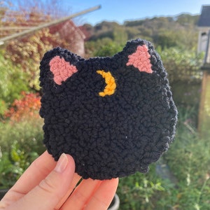 May include: Black crocheted cat with pink ears and a yellow crescent moon on its chest.