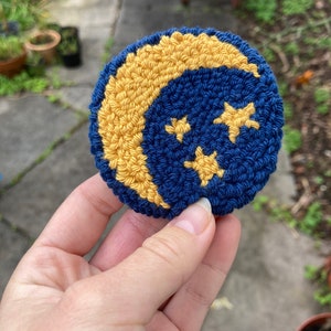 K&ouml;nnte beinhalten: Ein geh&auml;keltes Mond- und Sternen-Ornament in Blau und Gelb. Der Mond ist halbmondf&ouml;rmig und es befinden sich vier gelbe Sterne auf blauem Hintergrund.