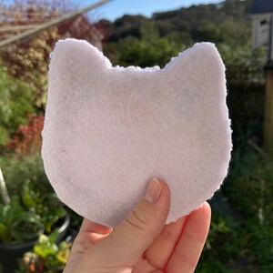 May include: White felt fabric cut in the shape of a cat's head, with two rounded ears.