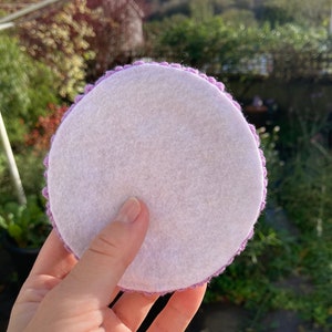 May include: A round, white felt coaster with a purple crocheted border.