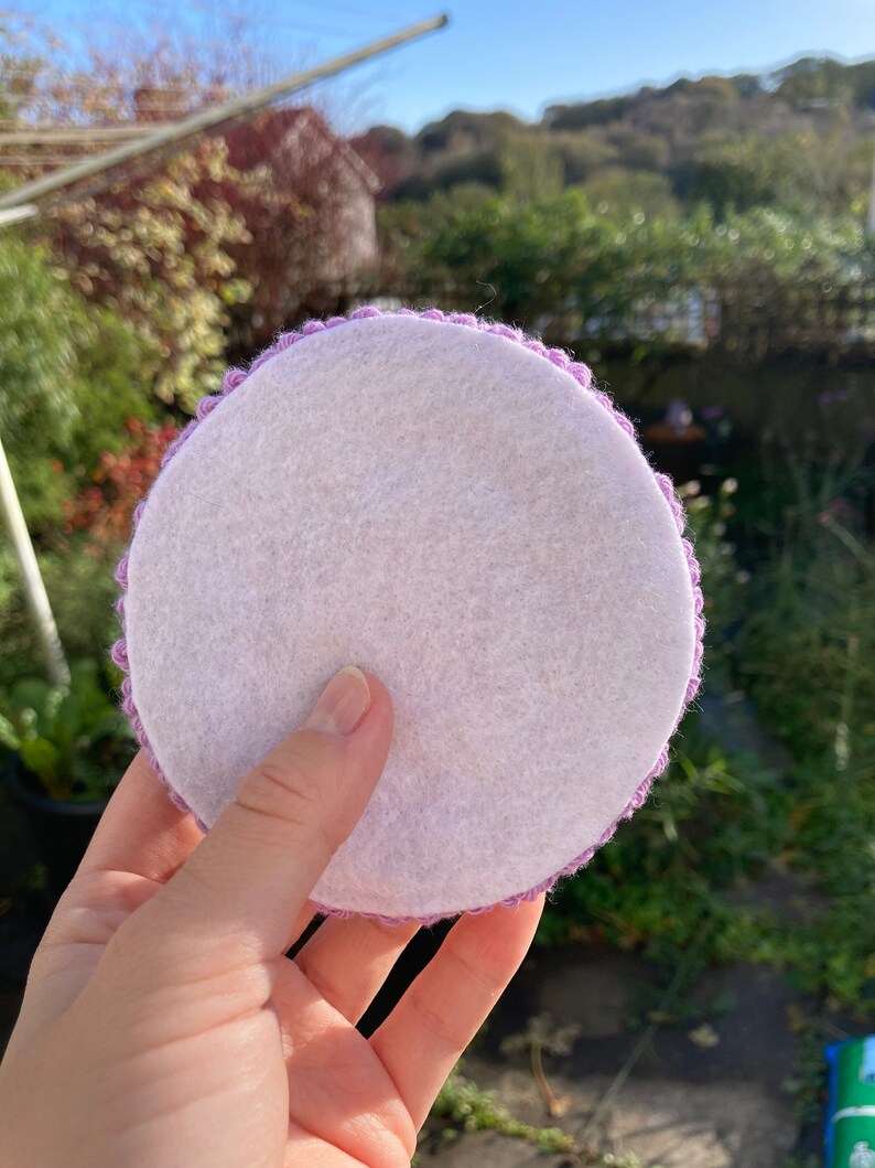 May include: A round, white felt coaster with a purple crocheted border.