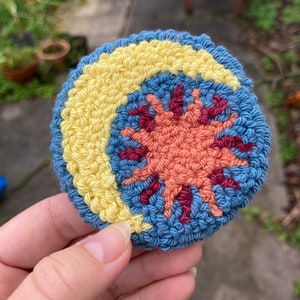 K&ouml;nnte beinhalten: Ein geh&auml;keltes Sonnen- und Monddesign in Blau, Gelb und Orange. Die Sonne befindet sich in der Mitte und hat ein Farbspiel aus Rot, Orange und Gelb. Der Mond ist halbmondf&ouml;rmig und gelb.