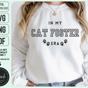 Könnte beinhalten: Weißer Pullover mit schwarzem Text, der "In My Cat Foster Era" lautet, mit Pfotenabdrücken auf beiden Seiten des Textes.