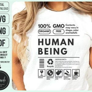 May include: White t-shirt with a graphic design that looks like a product label. The label says "100% GMO FREE ORGANIC" and "HUMAN BEING". The label also includes a list of ingredients and a recycle symbol.