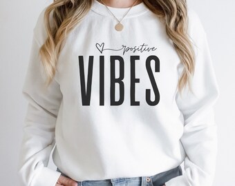 Peut inclure: Sweat-shirt blanc avec un texte noir qui dit "Positive Vibes" avec un petit symbole de cœur au-dessus du mot "Positive".
