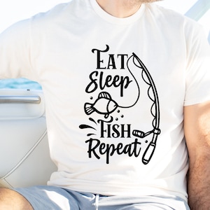 Puede incluir: Camiseta blanca con texto negro que dice "Eat Sleep Fish Repeat" y un gráfico de un pez y una caña de pescar.