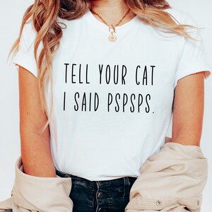 Puede incluir: Camiseta blanca con texto negro que dice "Dile a tu gato que dije pspsps."