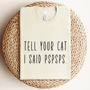 Puede incluir: Una camiseta verde claro con el texto "TELL YOUR CAT I SAID PSPSPS." impreso en negro.