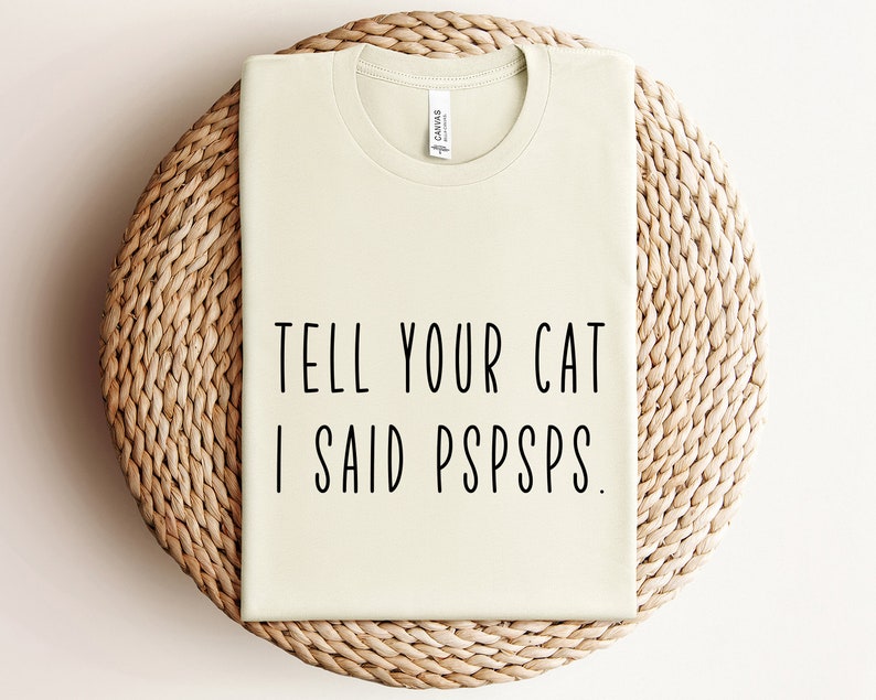 Puede incluir: Una camiseta verde claro con el texto "TELL YOUR CAT I SAID PSPSPS." impreso en negro.
