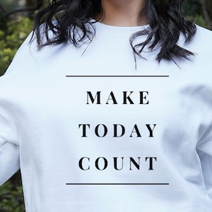 Puede incluir: Sudadera blanca con el texto "MAKE TODAY COUNT" impreso en negro.