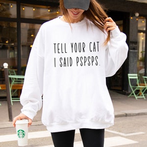 Puede incluir: Sudadera blanca con el texto "TELL YOUR CAT I SAID PSPSPS."