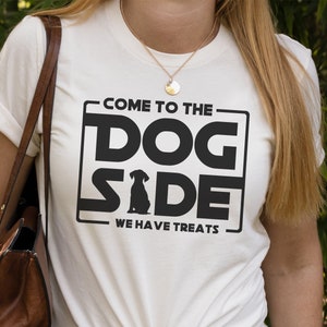 Könnte beinhalten: Weißes T-Shirt mit schwarzem Text, der "Come to the Dog Side We Have Treats" lautet. Der Text ist in einer von Star Wars inspirierten Schriftart gehalten. In der Mitte des Textes befindet sich eine Silhouette eines Hundes.