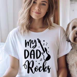 May include: White t-shirt with black text that reads "My Daddy Rocks" and a black silhouette of an electric guitar with musical notes and stars.
