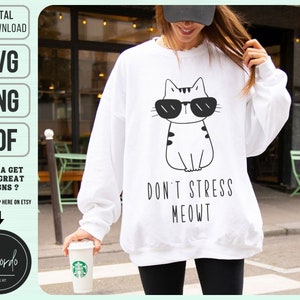 Può includere: Felpa bianca con un'illustrazione in bianco e nero di un gatto con occhiali da sole. Il testo "Don't Stress Meowt" è stampato sotto il gatto.