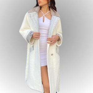 May include: An off-white long coat featuring a faux fur collar and snake-print detailing on the lapels, cuffs, and pockets. The coat has a double-breasted design with a decorative button. The coat is made of a soft, textured material.