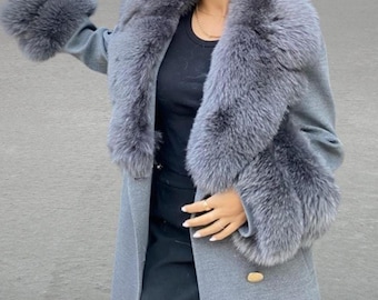 May include: A grey wool coat with a large grey fur collar and cuffs. The coat has a double breasted closure and a gold button.