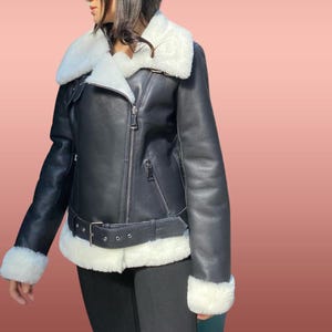 以下が含まれることがあります： 白いフェイクファーの襟とトリムが付いた黒い革のジャケット。ジャケットはジッパー留めとウエストにベルトが付いています。
