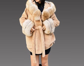 May include: A tan hooded coat with faux fur trim on the hood and cuffs. The coat has a matching belt and a soft, textured appearance. The coat is knee-length and appears warm and cozy.