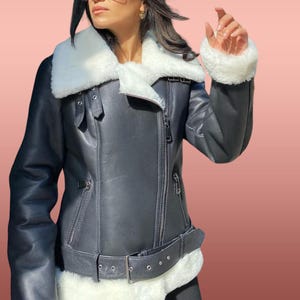 以下が含まれることがあります： 白いフェイクファーの襟と袖が付いた黒い革のジャケット。ジャケットはジッパーで閉じて、ウエストにベルトが付いています。