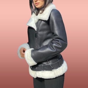 以下が含まれることがあります： 白いフェイクファーの襟とトリムが付いた黒い革のジャケット。ジャケットはジッパー留めとウエストにベルトが付いています。