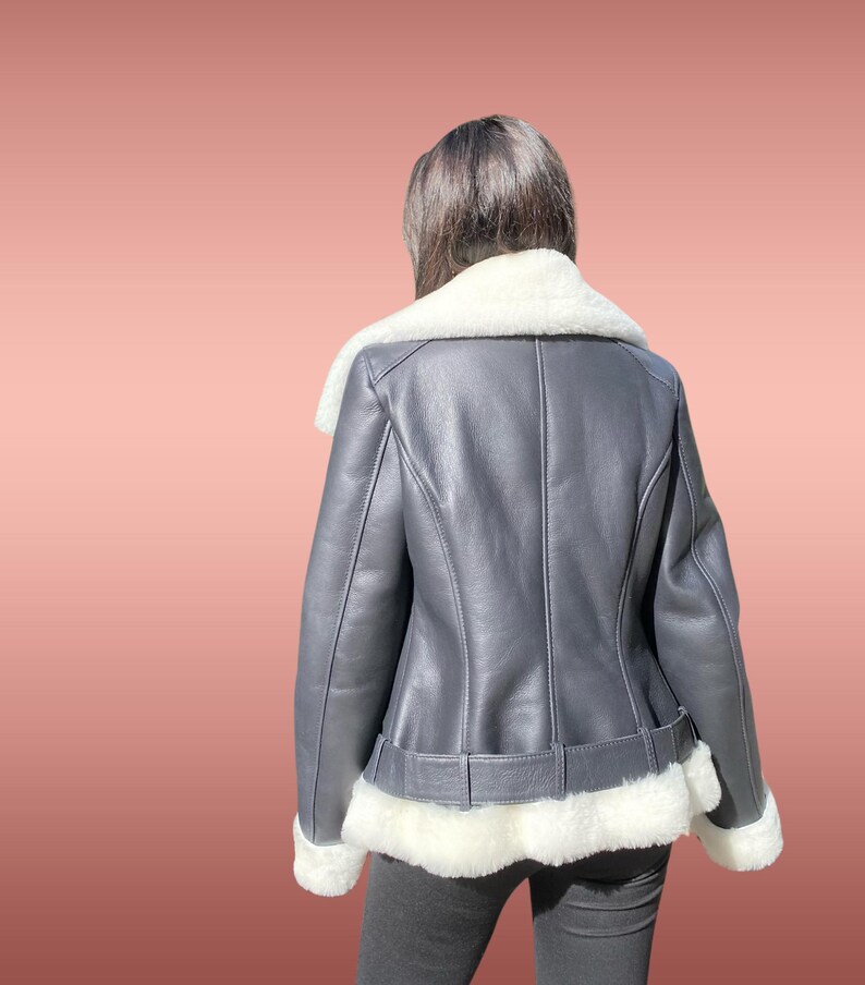以下が含まれることがあります： 白いシープスキン襟とトリムが付いた黒い革のジャケット。ジャケットはウエストにベルトが付いており、白いシープスキンで裏打ちされています。