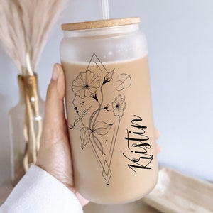 Pode incluir: Um copo de vidro fosco com tampa e canudo de bambu. O copo tem um design floral preto e branco com formas geom&eacute;tricas e o nome "Kristin" escrito em it&aacute;lico.