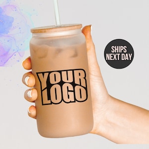 May include: A frosted glass tumbler with a bamboo lid and a straw. The tumbler is filled with iced coffee and has a black and white sticker that says "YOUR LOGO".