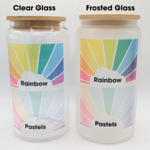 May include: Two glass jars with bamboo lids. The jar on the left is clear glass and the jar on the right is frosted glass. Both jars have a rainbow design with the words "Rainbow" and "Pastels" printed on them.