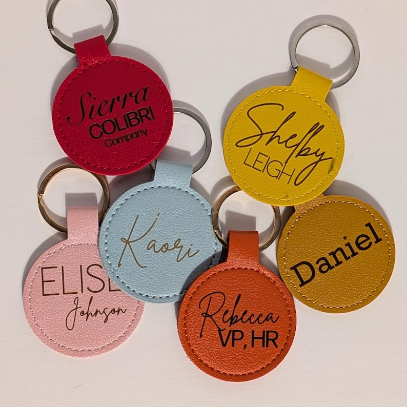 Puede incluir: Una colecci&oacute;n de coloridos llaveros con anillos plateados. Cada llavero es de un color diferente, incluyendo rojo, amarillo, naranja, rosa y azul. Los llaveros tienen nombres y nombres de empresas.