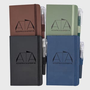 May include: Four rectangular notebooks in brown, green, black, and blue, each featuring an elastic closure band and a matching pen. The cover of each notebook is printed with the logo and text "ATA ACCOUNTING & TAX ADVISORY INC."