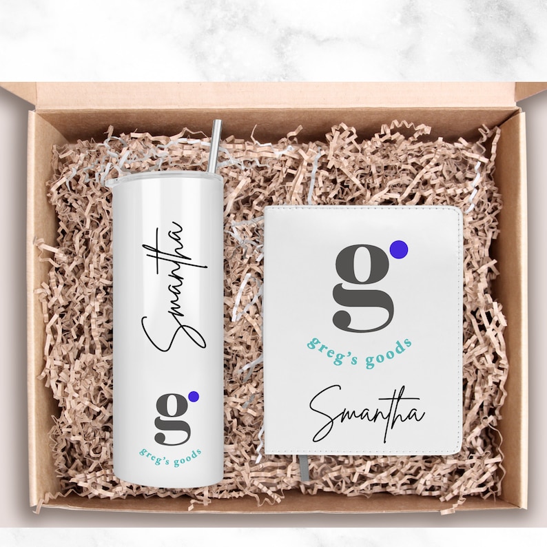 Pode incluir: Uma caixa de presente branca cheia de aparas de papel castanho cont&eacute;m um copo branco com um nome em it&aacute;lico preto "Samantha" e um logotipo "g" cinzento com o texto "greg's goods" em turquesa. A caixa tamb&eacute;m cont&eacute;m um caderno branco com o mesmo logotipo e o nome "Samantha" em it&aacute;lico preto.