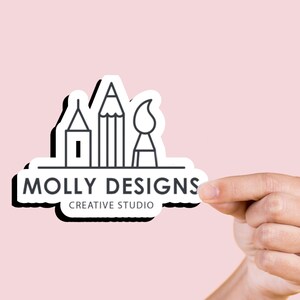 May include: A white sticker with a black outline and a logo for Molly Designs Creative Studio. The logo features a pencil, paintbrush, and a house, all in black outline.