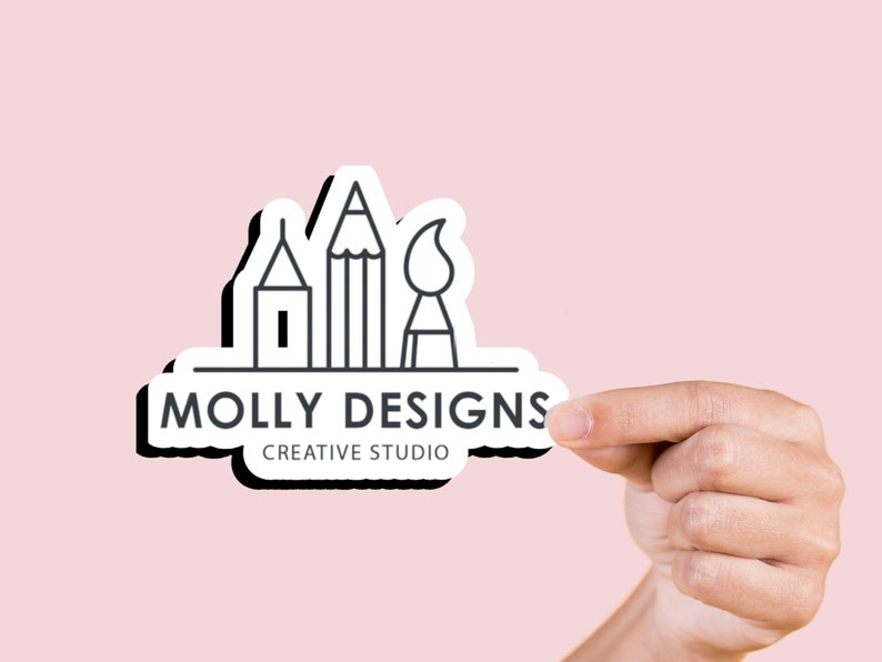May include: A white sticker with a black outline and a logo for Molly Designs Creative Studio. The logo features a pencil, paintbrush, and a house, all in black outline.