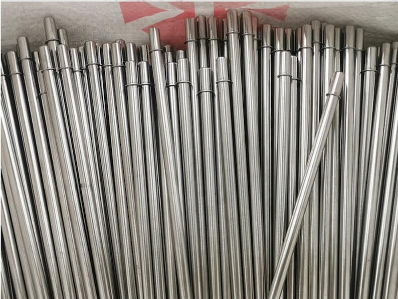 Op de afbeelding: Een bundel zilveren metalen drinkrietjes. De rietjes zijn waaiervormig gerangschikt, met de uiteinden van de rietjes die naar de bovenkant van de afbeelding wijzen.