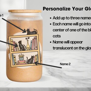 May include: A personalised glass featuring a bookshelf design with three black cats. The glass has a brown background and a bamboo lid. The text "Personalize Your Glass" is at the top of the image. The text "Add up to three names" is below the title. The text "Each name will go into the centre of one of the black cats" is below the first line of text. The text "Name will appear translucent on the glass" is below the second line of text. The text "Name 1" is above the top cat. The text "Name 2" is below the bottom cat. The text "Name 3" is to the left of the middle cat. The names of the cats are "Olle", "Anka", and "Smy".