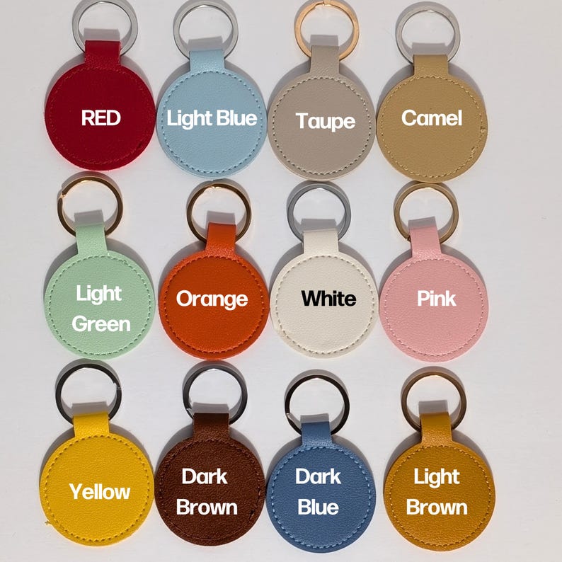Puede incluir: Una colecci&oacute;n de llaveros redondos en varios colores, cada uno con un llavero plateado o dorado. Los colores incluyen rojo, azul claro, taupe, camel, verde claro, naranja, blanco, rosa, amarillo, marr&oacute;n oscuro, azul oscuro y marr&oacute;n claro. Cada llavero tiene el nombre del color impreso.