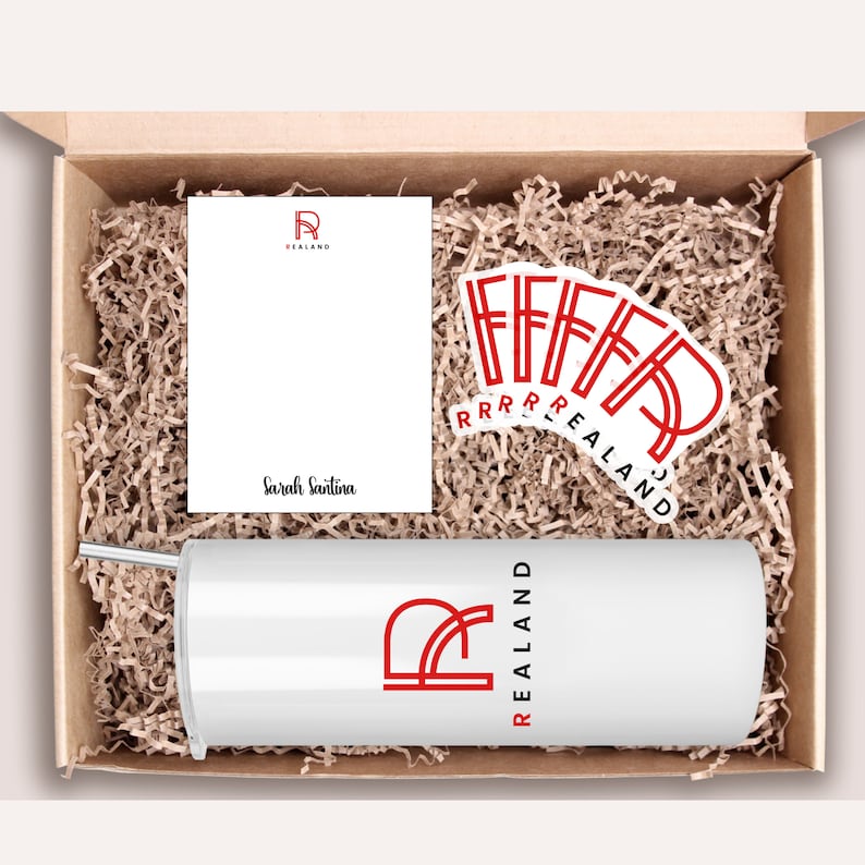 Peut inclure: Une bo&icirc;te cadeau blanche remplie de papier d'emballage brun. La bo&icirc;te contient un gobelet blanc avec un logo rouge qui dit "REALAND". Il y a aussi une carte blanche avec le m&ecirc;me logo et le nom "Sarah Santina" &eacute;crit dessus. Il y a plusieurs autocollants rouges avec le m&ecirc;me logo.