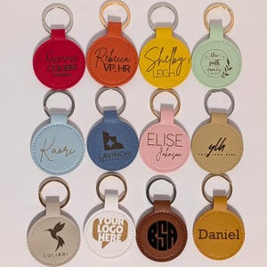 Puede incluir: Una colecci&oacute;n de llaveros redondos personalizados en varios colores, incluyendo rojo, naranja, amarillo y azul. Cada llavero presenta texto o logotipos personalizados, como nombres, iniciales y logotipos de empresas, sujetos a un llavero plateado.