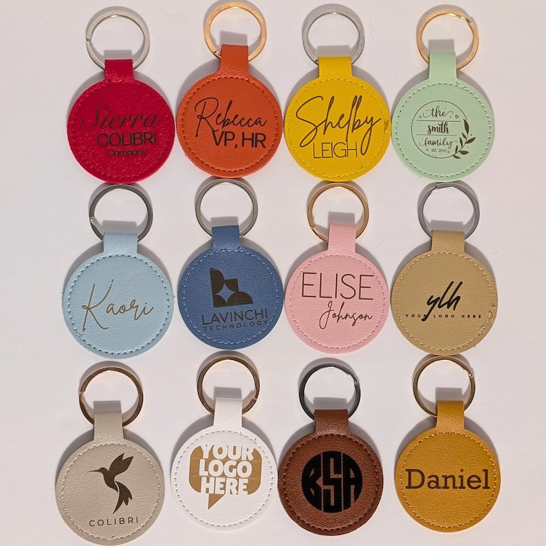 Puede incluir: Una colecci&oacute;n de llaveros redondos personalizados en varios colores, incluyendo rojo, naranja, amarillo y azul. Cada llavero presenta texto o logotipos personalizados, como nombres, iniciales y logotipos de empresas, sujetos a un llavero plateado.