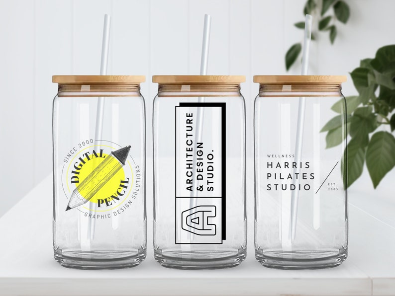 Pode incluir: Tr&ecirc;s copos de vidro transparentes com tampas de bambu e canudos brancos. Os copos t&ecirc;m diferentes logotipos impressos neles: "Digital Pencil Graphic Design Solutions", "Architecture & Design Studio" e "Wellness Harris Pilates Studio".
