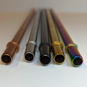 Op de afbeelding: Vijf herbruikbare metalen drinkrietjes in verschillende kleuren: koper, zilver, zwart, goud en regenboogkleurig.