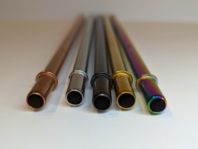 Op de afbeelding: Vijf herbruikbare metalen drinkrietjes in verschillende kleuren: koper, zilver, zwart, goud en regenboogkleurig.