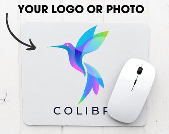 May include: A white mouse pad with a colorful hummingbird design and the text "COLIBRI" in blue. A white wireless mouse is on the mouse pad.