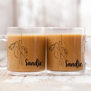 May include: Two clear glass mugs with black handles. Each mug has a black and white illustration of a flower with the name "Sandie" printed below.