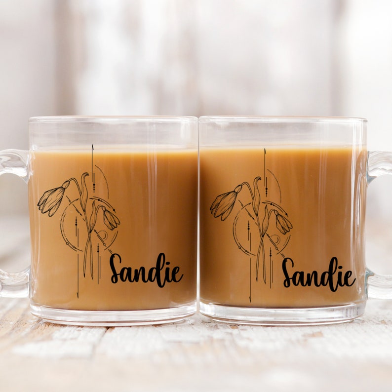 May include: Two clear glass mugs with black handles. Each mug has a black and white illustration of a flower with the name "Sandie" printed below.
