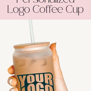 Pode incluir: Uma caneca de caf&eacute; de vidro fosco marrom com tampa de bambu e um canudo. A caneca tem um gr&aacute;fico preto e branco que diz "YOUR LOGO".