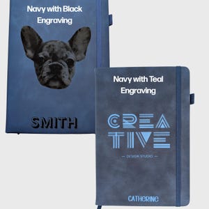 May include: Two navy blue notebooks with elastic closures. The left notebook features a black engraved French bulldog portrait and the name SMITH. The right notebook displays the word CREATIVE, the text DESIGN STUDIO, and the name CATHERINE in teal.