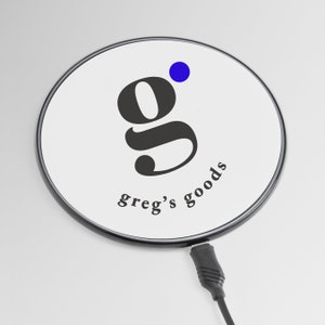 May include: A black and white logo with the letter "g" and the text "greg's goods" on a white round wireless charging pad with a black border. The charging pad is connected to a black charging cable.